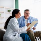Young doctor asking senior impaired male patient in wheelchair to sign insurance policy at home. Handicapped elderly man putting his signature under surgery consent form, reading medical document